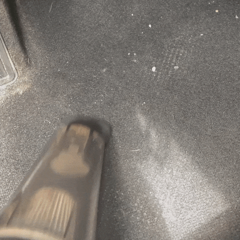The vacuum in action, sucking up dirt and rocks from the writer's driver's seat floor in a car.