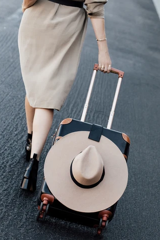 A model rolling a suitcase, with the luggage tag securely holding a wide-brim hat.