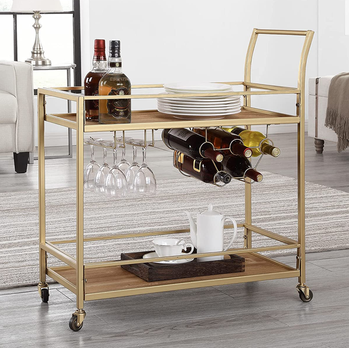 A gold bar cart filled with glasses, bottles, plates, and a tea set.