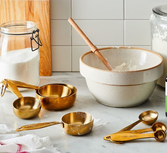 Gold measuring cups and spoons placed on a counter beside a mixing bowl and baking ingredients, exuding charm and practicality.