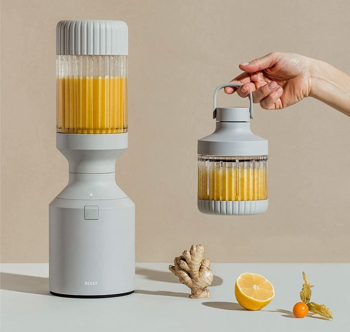 A gray blender filled with a vibrant orange smoothie, accompanied by a smaller blending container with a convenient carry handle.