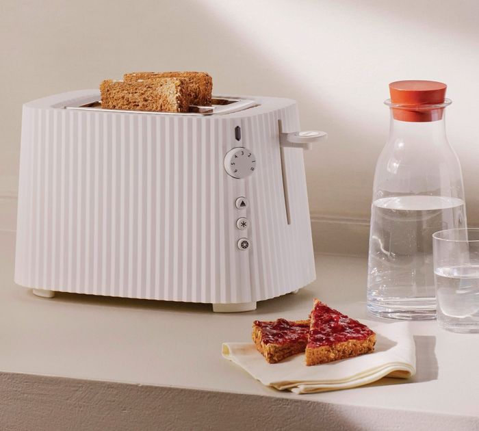 The white pleated toaster with two pieces of toast, placed beside jam-covered toast and a glass of water.