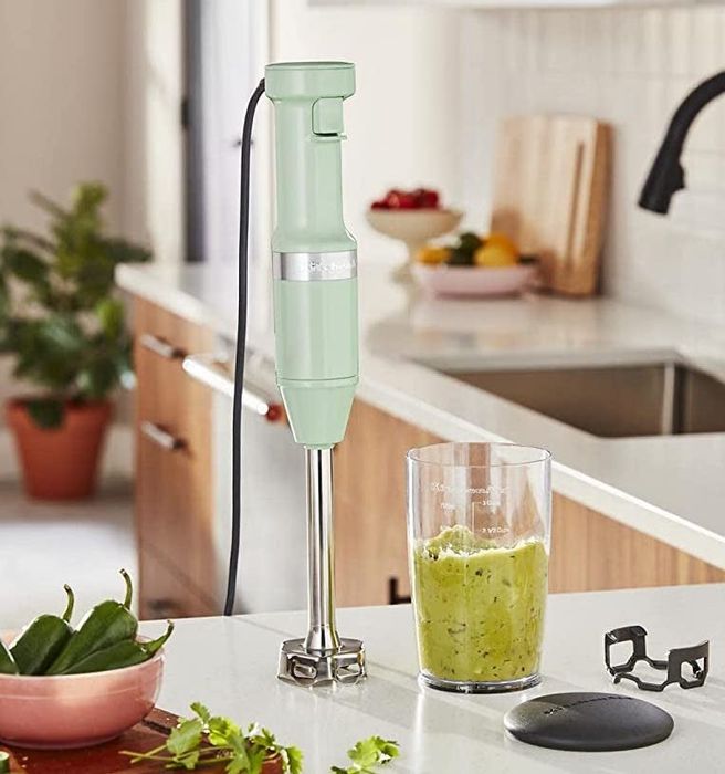 A light green immersion blender resting on the counter beside a bowl of guacamole.
