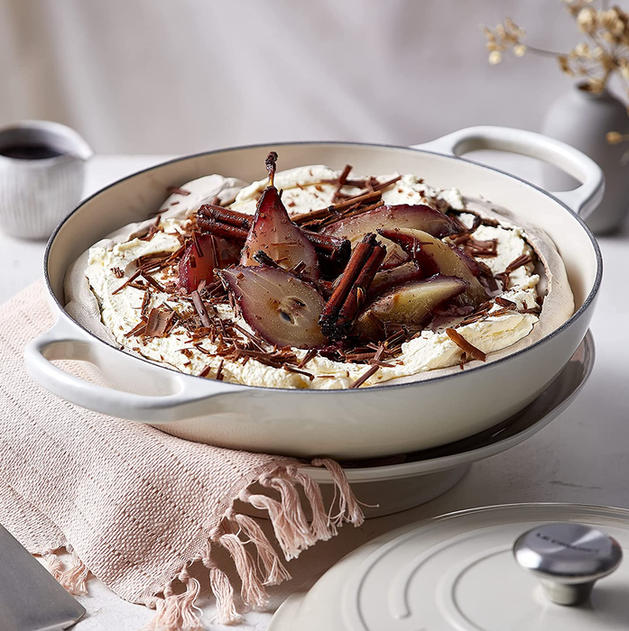 A white braiser gracefully holding a dessert of pears.