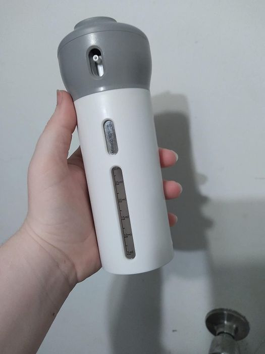A reviewer holds the dispenser, showing its size, which is about the same as a small water bottle.