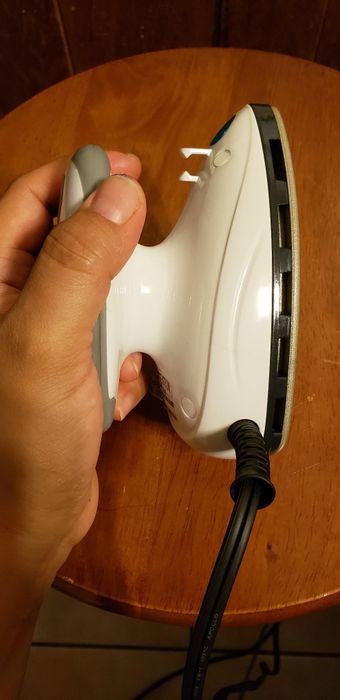 A reviewer holds the mini iron to the side, giving a clear view of its small size.