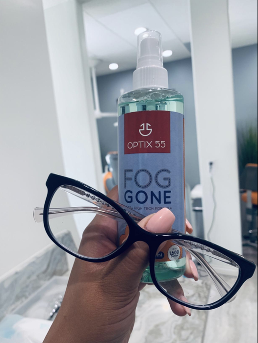 A reviewer holding up glasses alongside a bottle of anti-fog spray