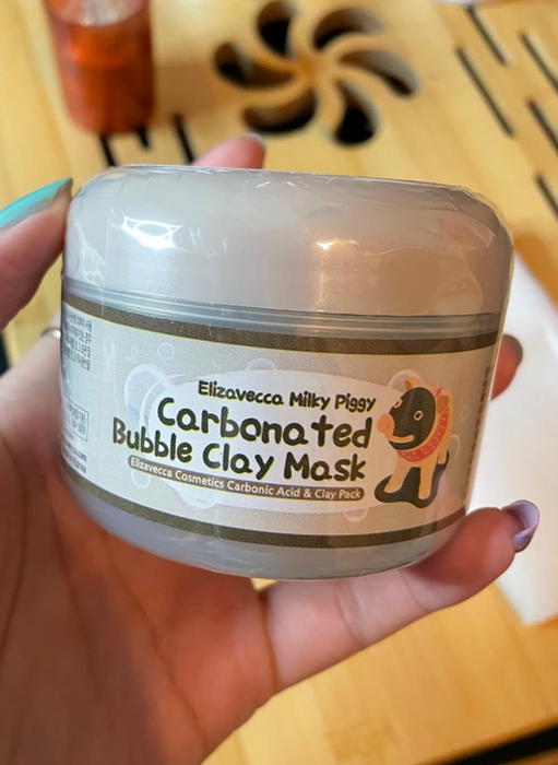 A reviewer holding a container of the clay mask.