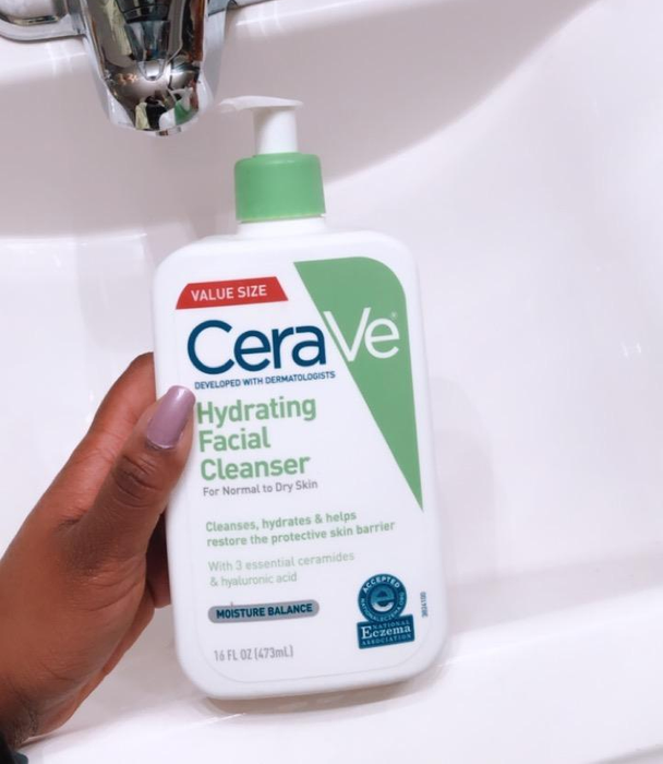 A reviewer holding the bottle of CeraVe's white and green hydrating cleanser.