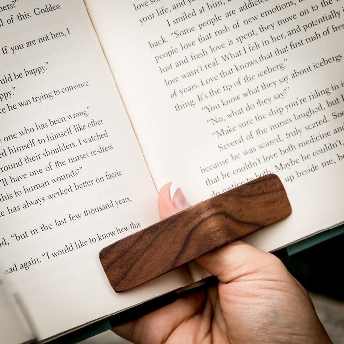 A thumb hooked into a rectangular wooden page holder, keeping a book open