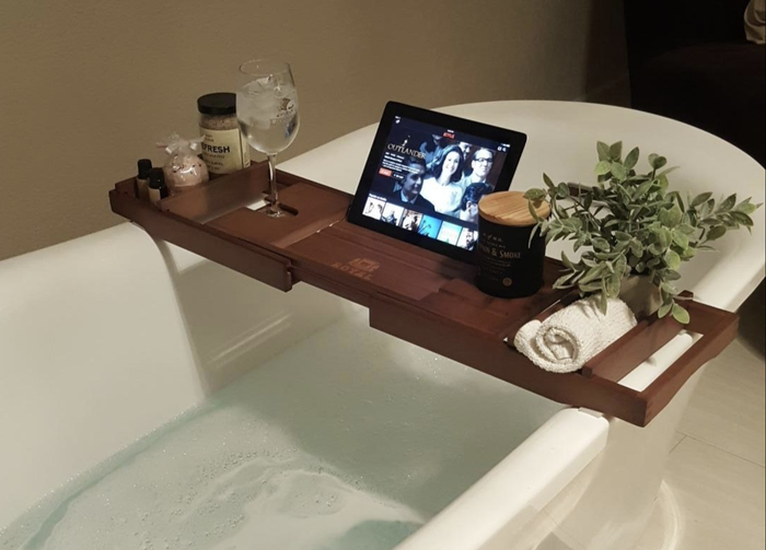 Reviewer image displaying a wooden bath caddy holding an iPad, washcloth, plant, candle, wine glass, and bath salts