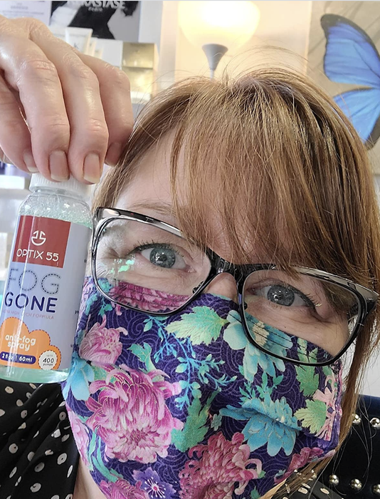A reviewer showing a bottle of spray with their glasses and face mask unfogged
