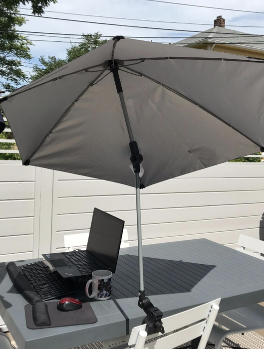 A white umbrella clamped onto a chair, providing shade to a laptop on a table