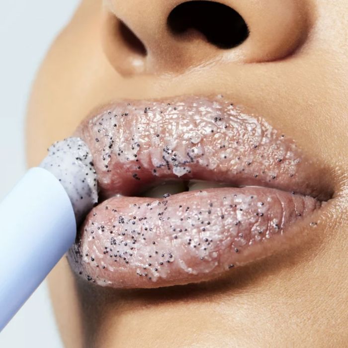 A person gently applying a lip exfoliator to their lips
