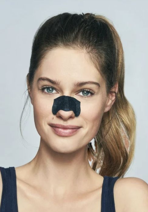 A person applying a nose strip to remove impurities.
