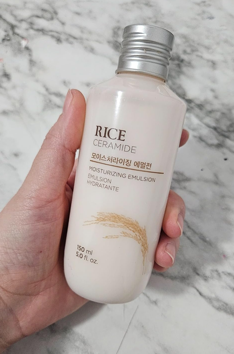 A hand holding a bottle of Rice Ceramide Moisturizing Emulsion skincare product.