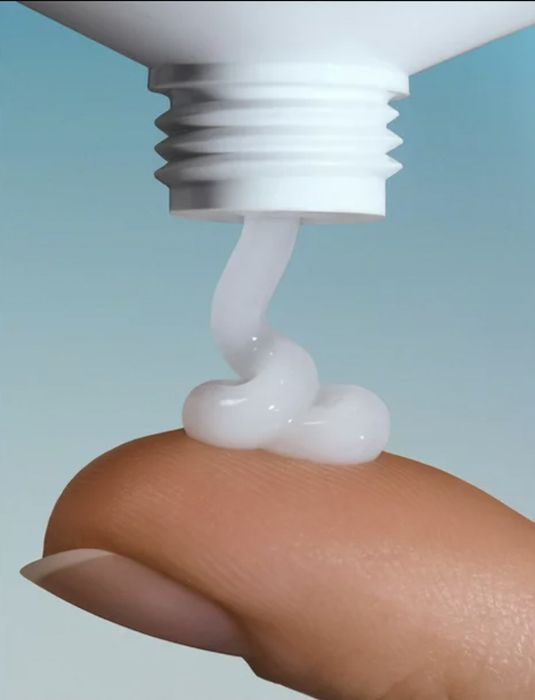 A person dispensing face cream onto their finger.