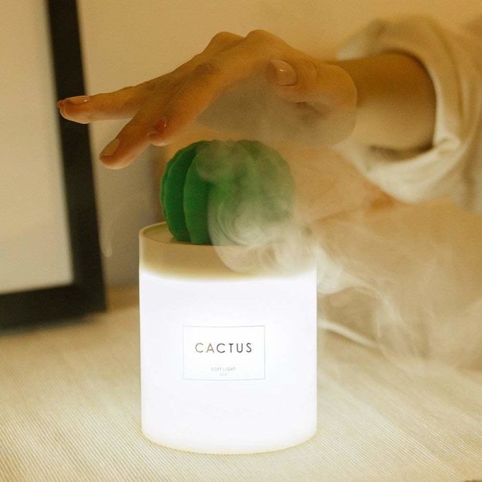 A small white humidifier with a tiny green cactus sprouting from it, glowing gently.