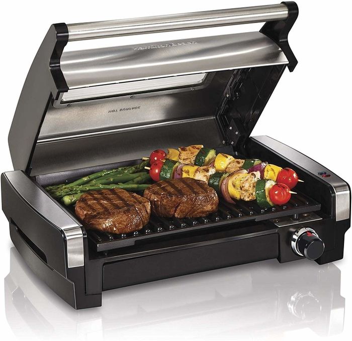 A small grill sizzling two burgers alongside corn and asparagus, perfect for a quick outdoor meal.