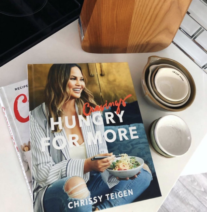 The cover of Chrissy Teigen's *Cravings: Hungry for More* book, featuring her happily enjoying a salad while smiling.