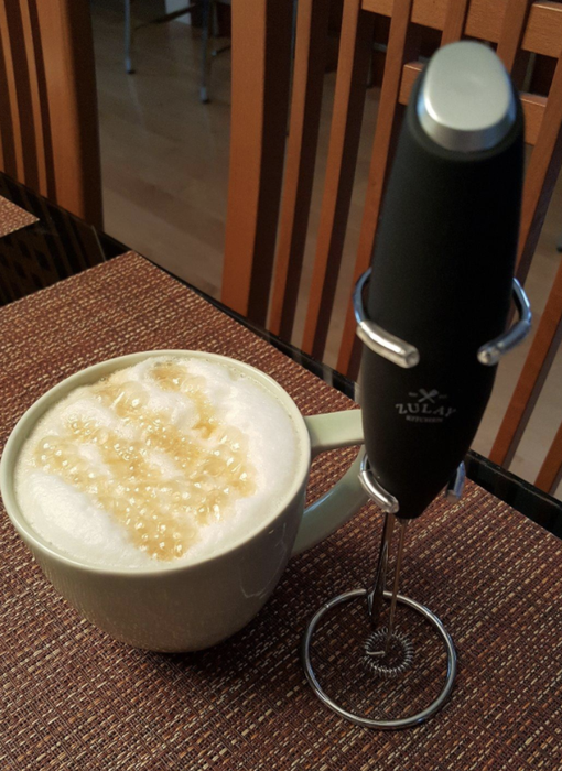 a sleek black handheld frother beside a cup of coffee topped with frothy milk