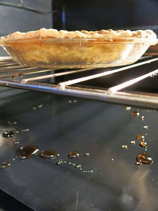 A freshly baked pie in the oven, with juices spilling over and dripping onto the protective mat below.