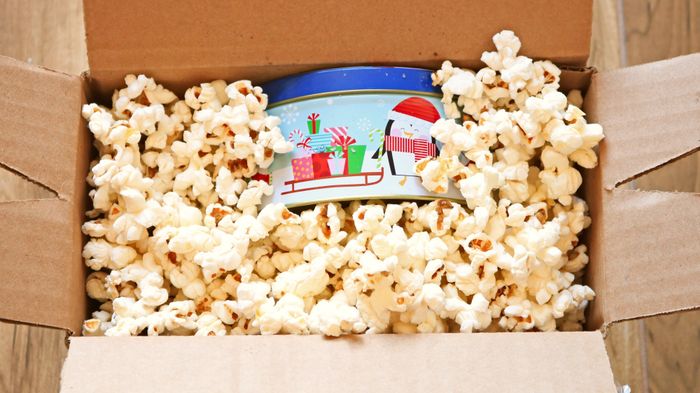 A cookie tin inside a box filled with popcorn.
