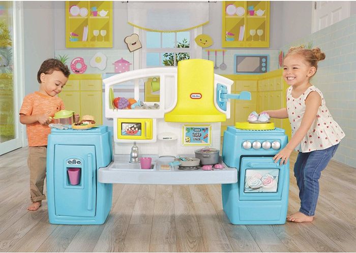 Two kids happily playing with their toy kitchen, pretending to cook.