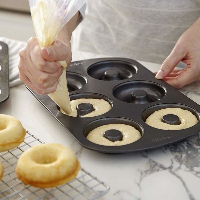 A person piping batter into donut molds within a pan.