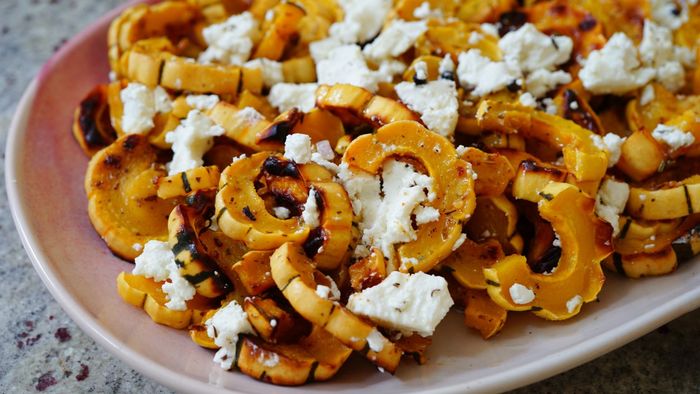A plate of delicately sliced delicata squash topped with white cheese.