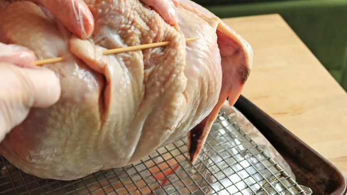 A skewer is inserted through the neck skin of the turkey, connecting it to the body.
