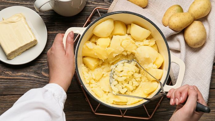 A person is holding a potato masher and mashing a pot of potatoes.