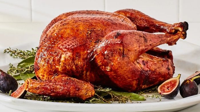 A beautifully roasted turkey served on a white plate, surrounded by figs and fresh herbs at the base.