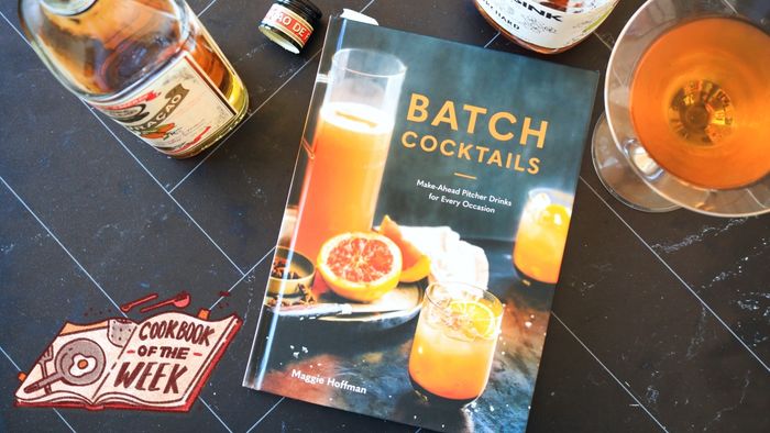 A photo of the Batch Cocktails cookbook placed on a table alongside two bottles of liquor and a prepared cocktail.