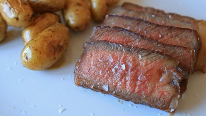 Sliced steak served alongside baby potatoes on a dish.