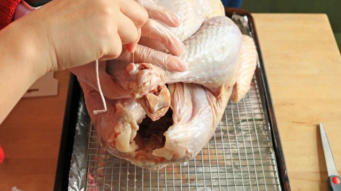 A hand wrapping the kitchen string around the turkey's legs.