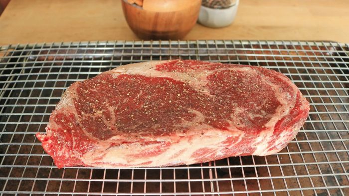 A raw steak resting on a wire rack set over a baking sheet.