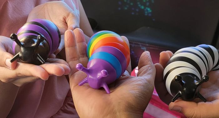Hands holding a set of toy slugs with different patterns: purple and black stripes, rainbow stripes, and black and white stripes.