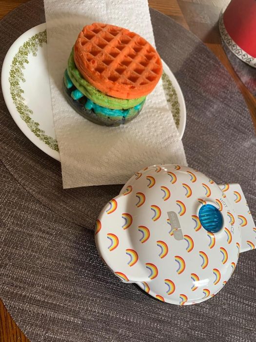 Reviewers are loving the white and rainbow waffle maker, shown here next to a plate of beautifully colorful waffles.