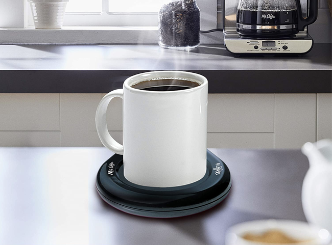 A cup of coffee resting on top of a sleek black, round heated plate
