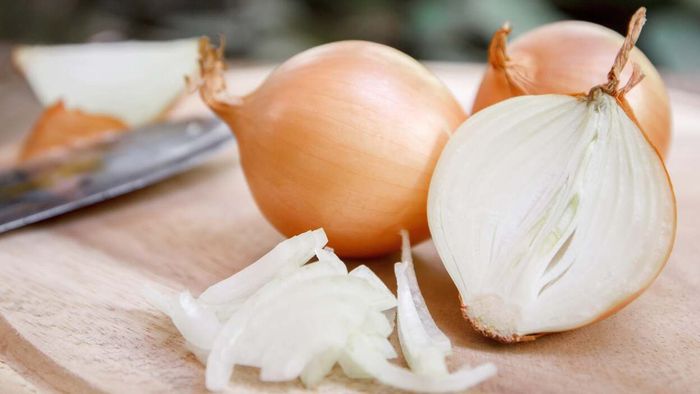 A white onion sliced in half, resting on a wooden table in an outdoor setting.