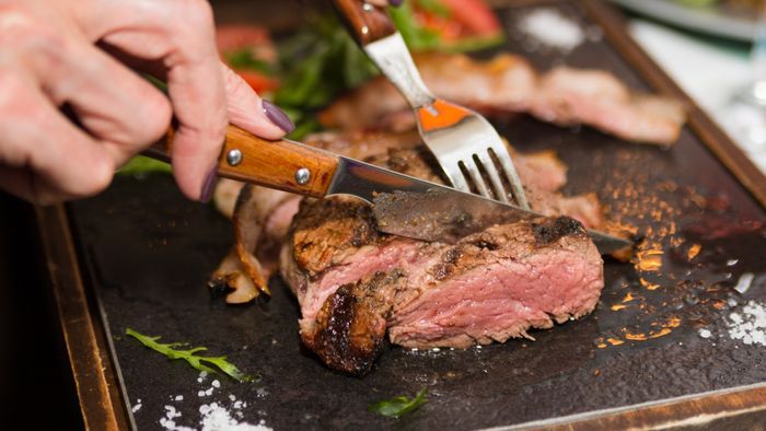 A woman using a steak knife to cut through a steak.