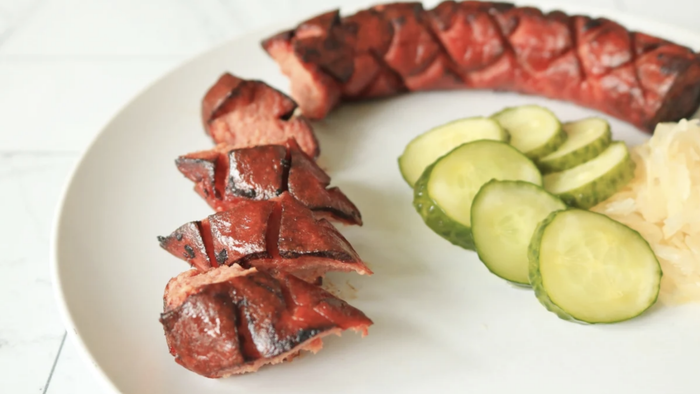 Sliced kielbasa served with pickles and sauerkraut on a plate.