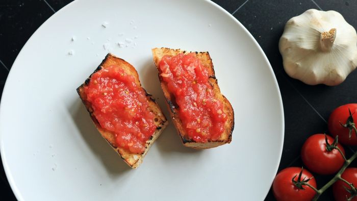 Two slices of pan con tomate served on a white plate.