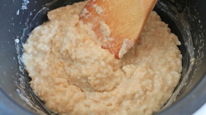 A bowl of cooked oatmeal resting in a container, accompanied by a wooden spoon.