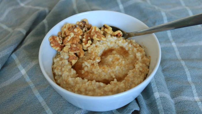 A bowl of steel-cut oats drizzled with honey and sprinkled with walnuts rests on a patterned tablecloth.