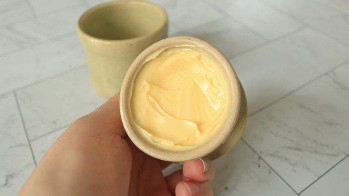 A hand holding a lid with the butter cup filled.