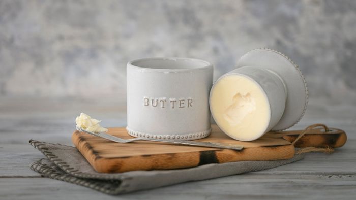 A butter keeper placed on a table next to a butter knife.
