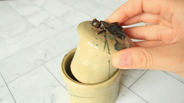 A hand lifting the lid off a butter keeper.