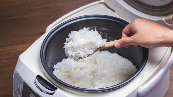 A hand carefully scooping rice from a rice cooker.